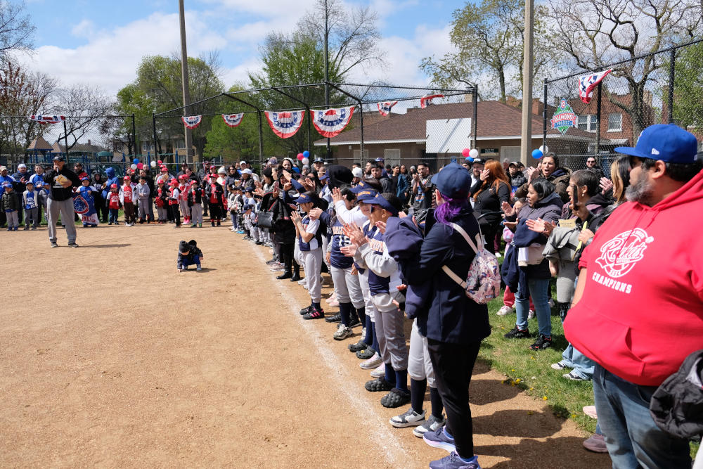 Players, parents, coaches and guests watch Omega Delta Youth Baseball & Softball League chief Danny Gaichas introduce the 20th season of play at Chicago's Hoyne Park.